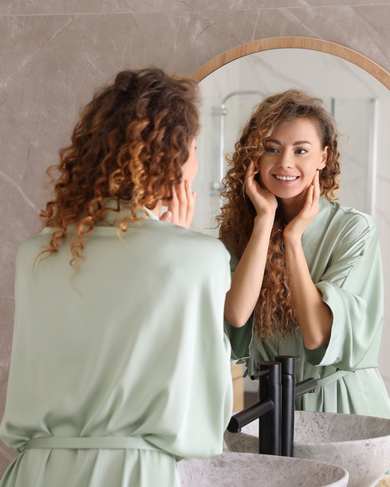 A woman looking in a mirror at her smile with her clear aligners.